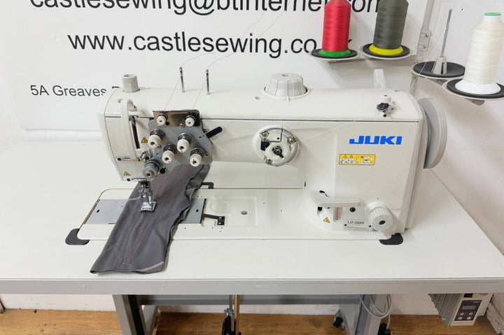 Sewing machine on a table with spools of thread in the background, featuring the Juki brand.